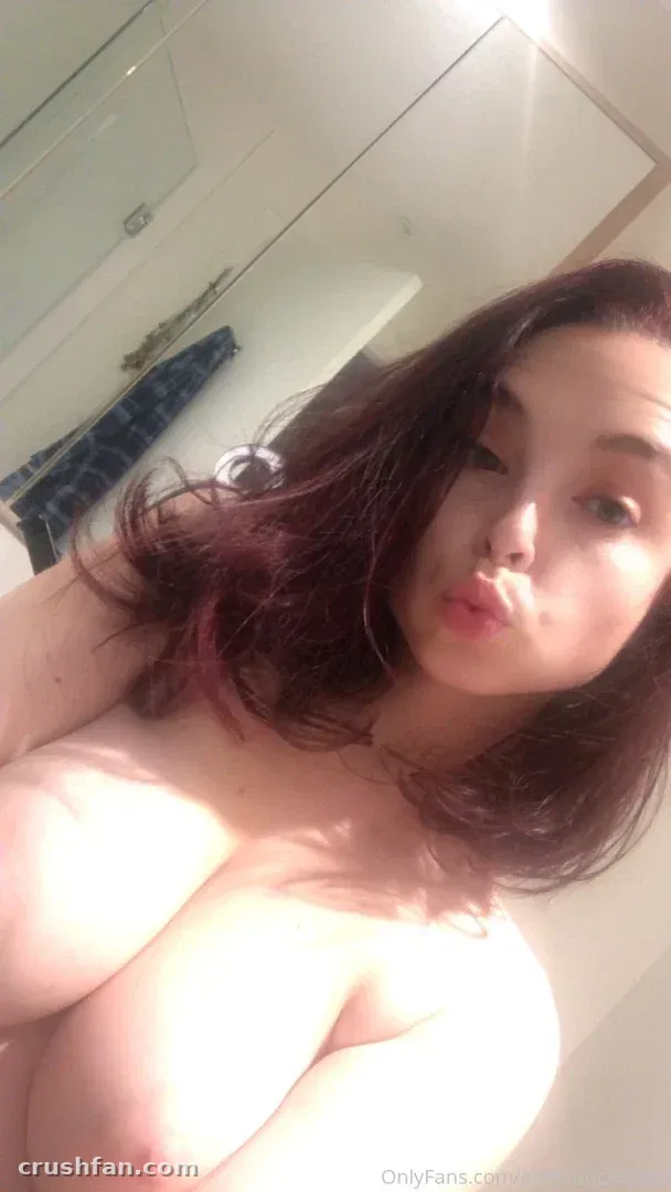 Creator with long dark hair taking a playful close-up selfie in a bright bathroom.