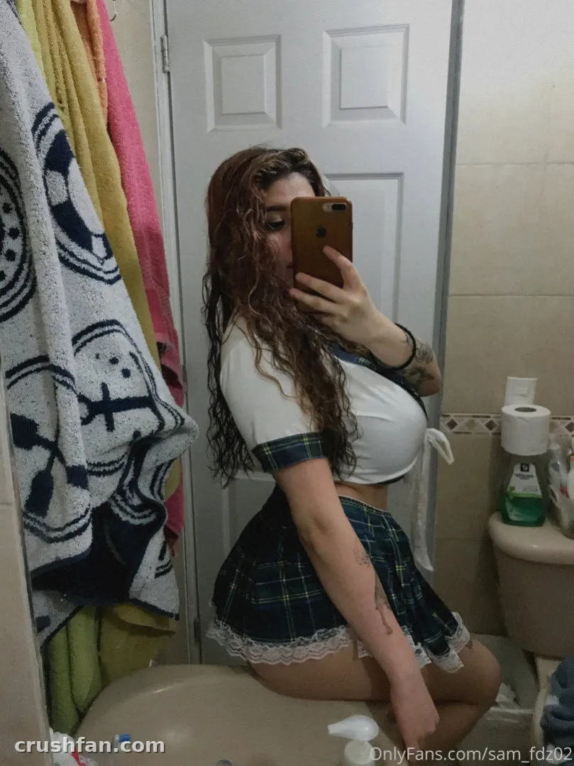 Paulin con un top corto blanco y falda de cuadros tomándose una selfie frente al espejo del baño
