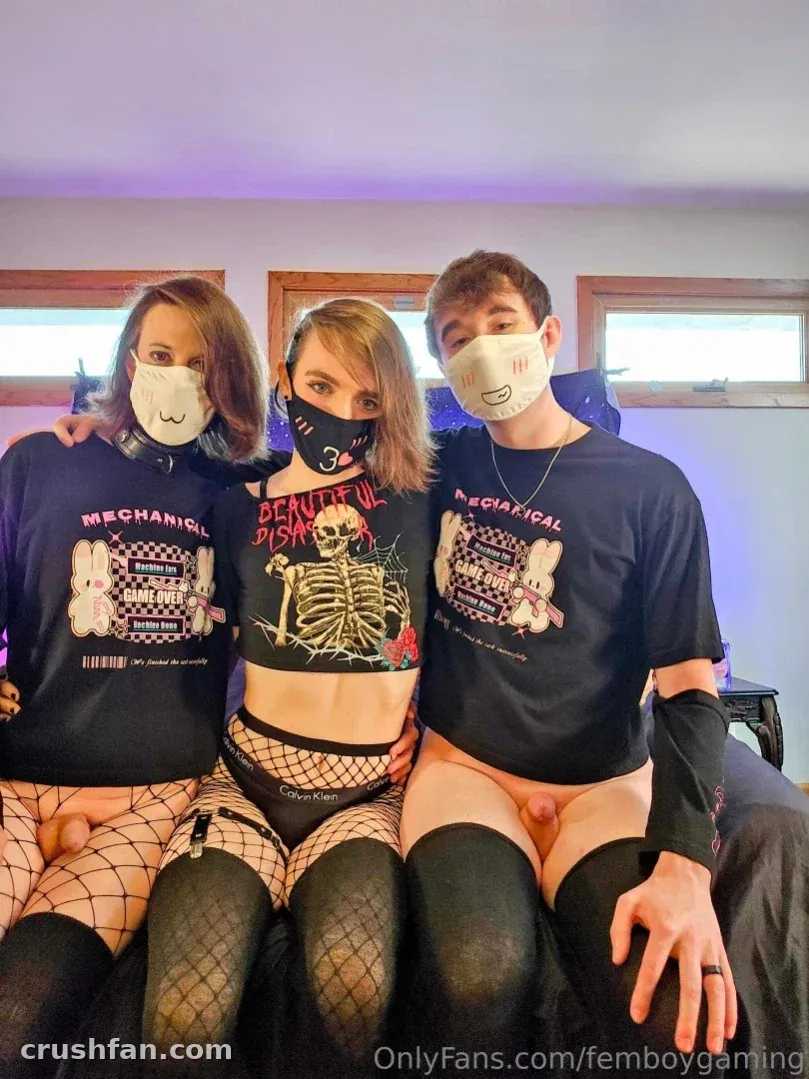 Femboy_Gaming seated with two companions in graphic tops and face masks indoors.