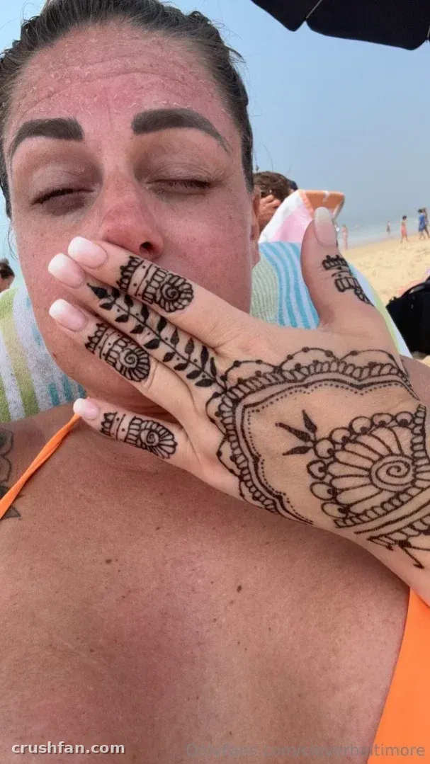 Cloverbaltimore mit Henna-Handkunst und orangefarbenem Bikini am Strand.