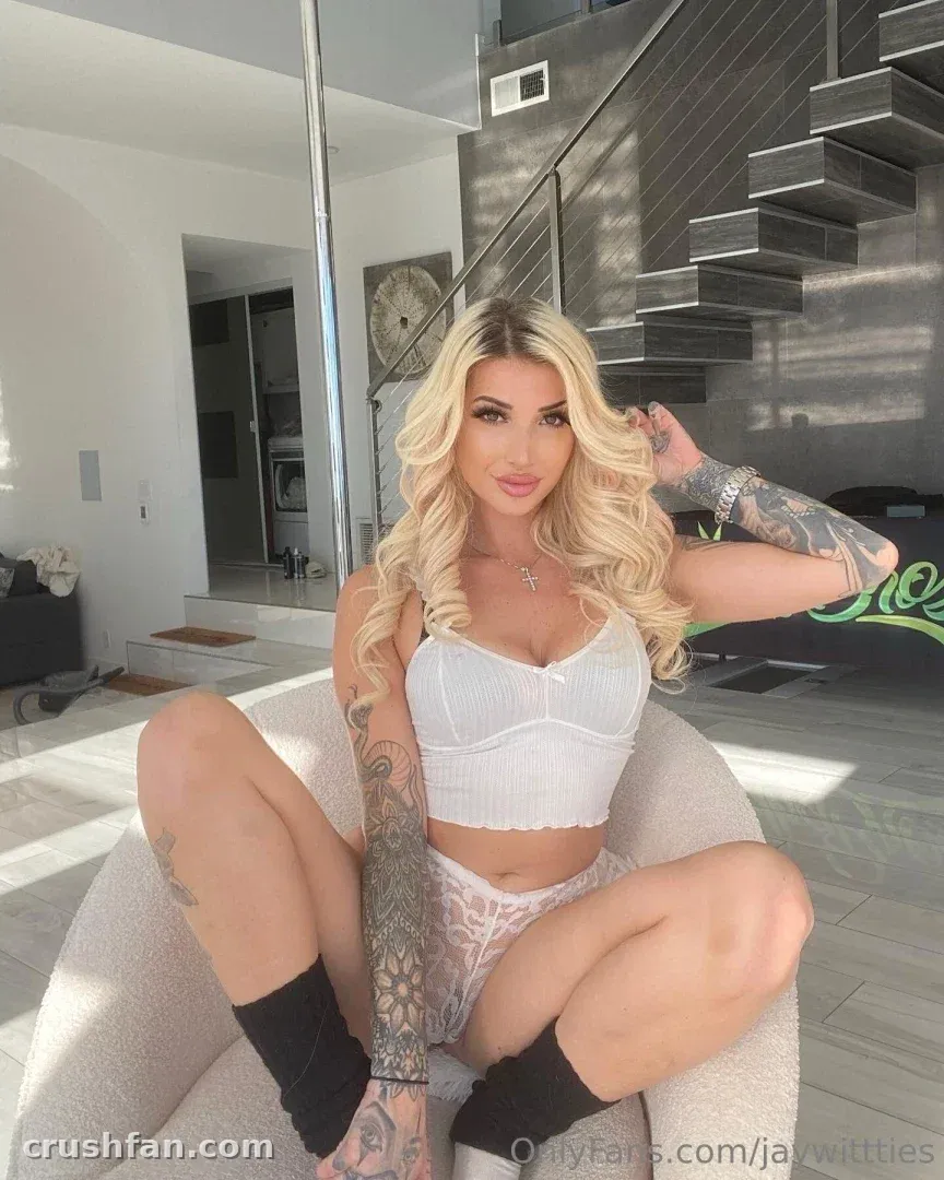 jaywittties in a white crop top and bottoms sitting on a cream chair in a modern room