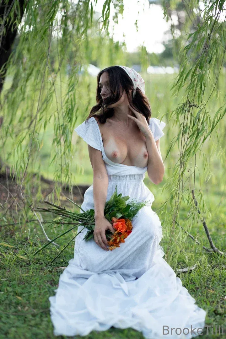 Femme en robe blanche agenouillée parmi des branches de saule tenant des fleurs orange