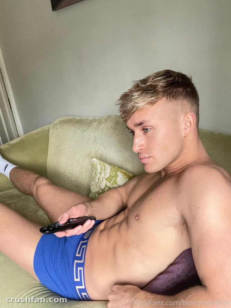 Creator reclining on a green sofa in blue briefs holding a remote