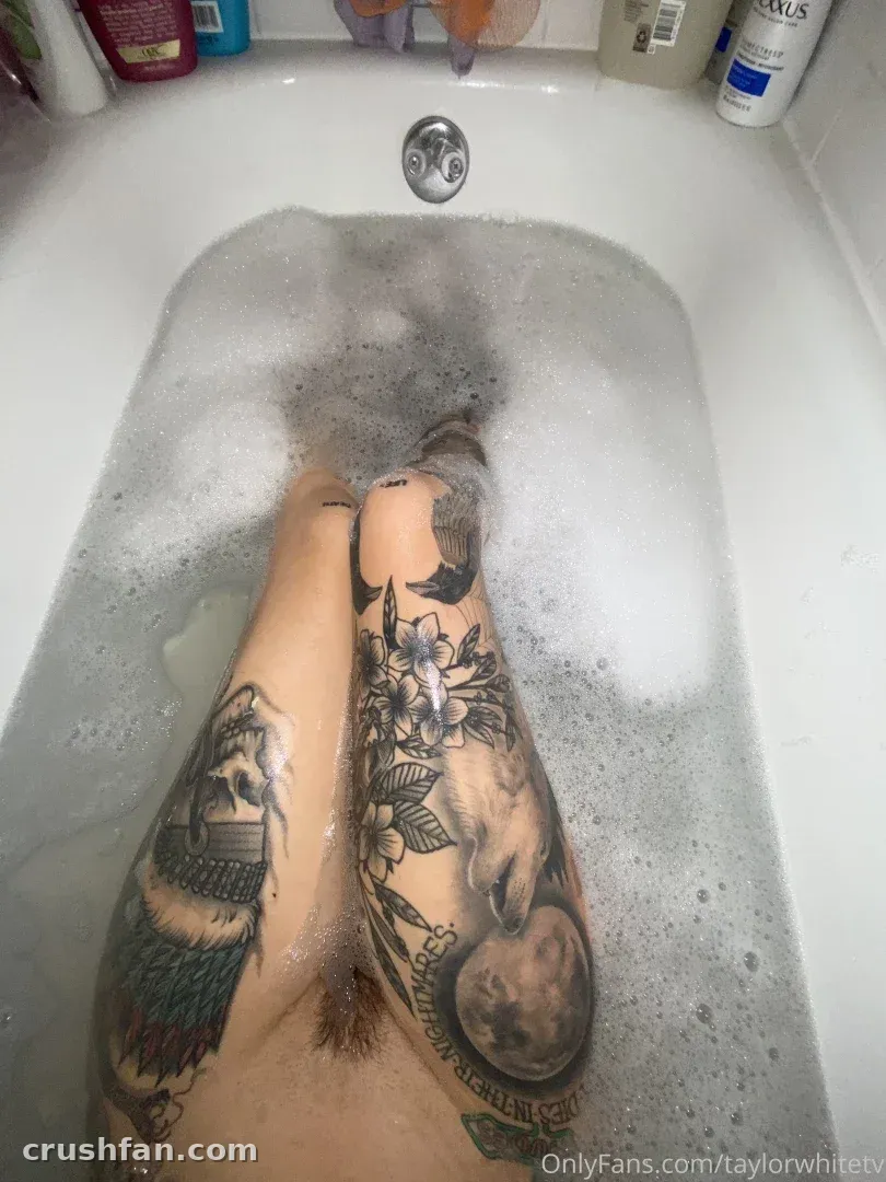 Taylor white em um banho de espuma com as pernas tatuadas visíveis de cima.