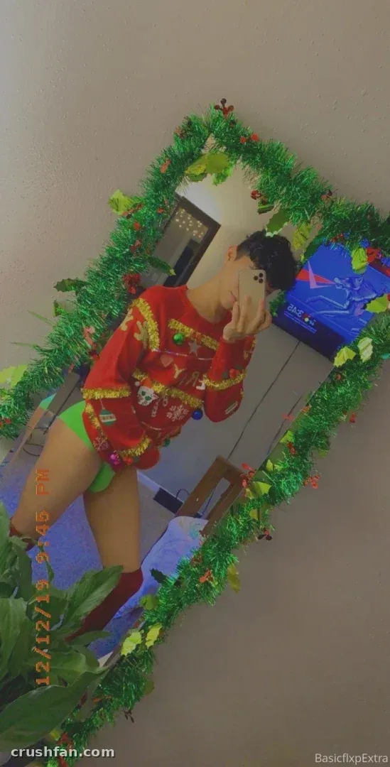 Extra Content com um suéter natalino vermelho e cueca verde tirando uma selfie no espelho com guirlanda.
