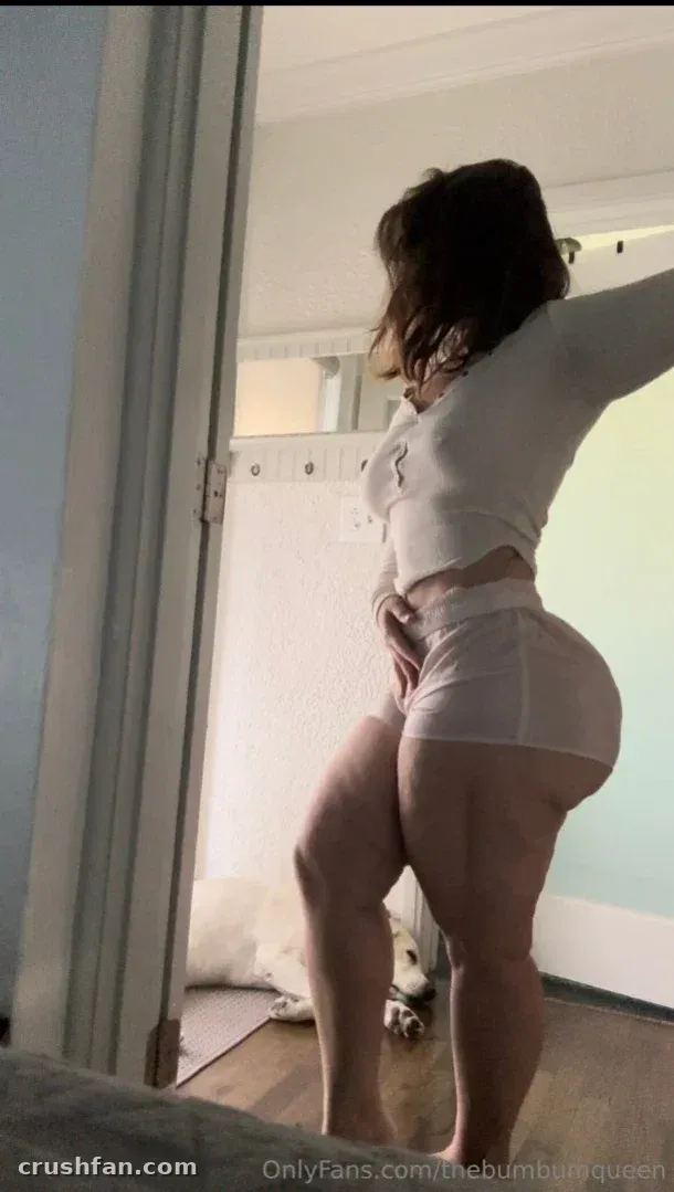 TheBumbumqueen en haut court et short blancs posant près d'une porte en intérieur
