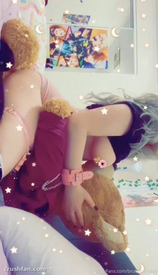Creator in rosa Outfit auf einem Bett mit einem Teddybären, mit Stern-Overlays und einem Spiegel im Hintergrund.
