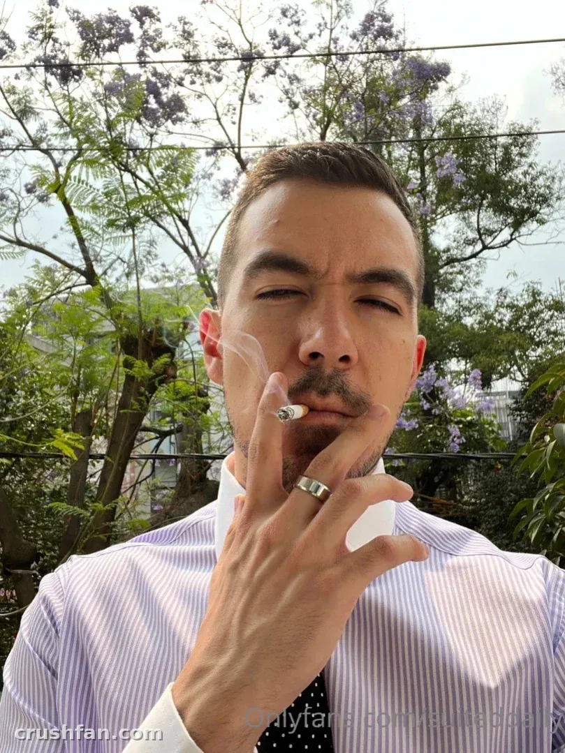 Suited Daily in a striped shirt outdoors with purple blossoms behind him