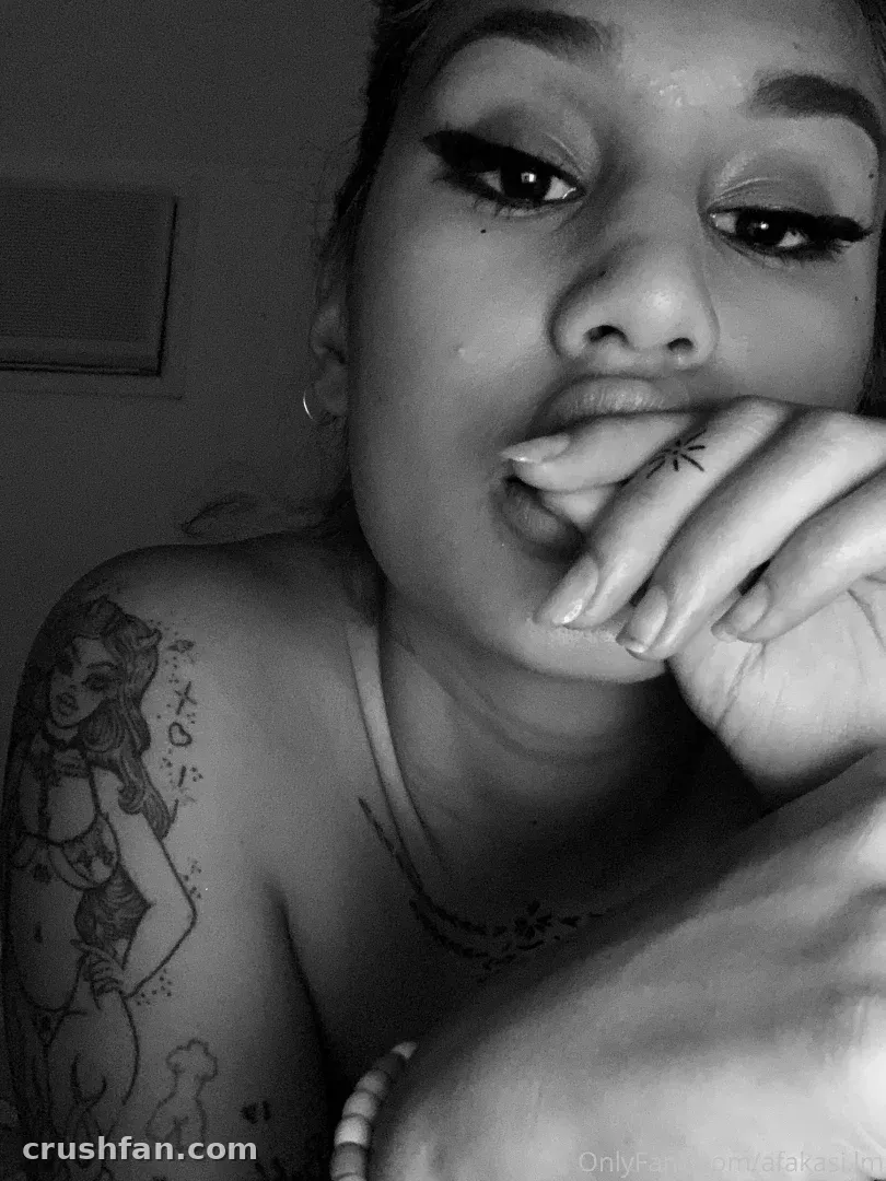Black and white close portrait of Nesian Tink resting her chin on her hand, showing arm tattoos
