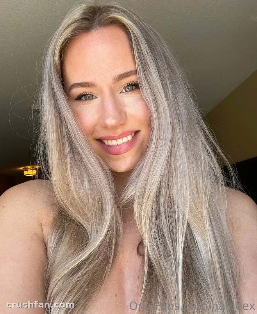 Hayleex tirando uma selfie interna de perto com longos cabelos loiro-prateados e um sorriso suave