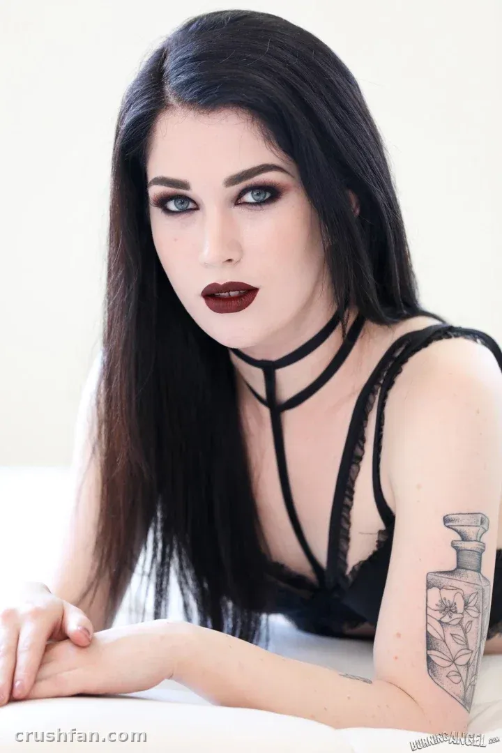 Evelyn Claire en dentelle noire avec un collier, se penchant en avant dans une pièce lumineuse.