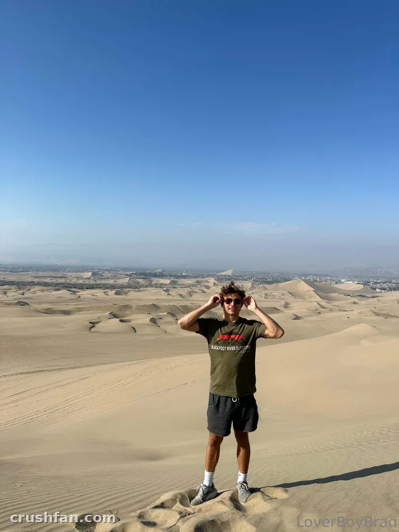 Leo in an olive t-shirt and shorts standing on sand dunes under a blue sky