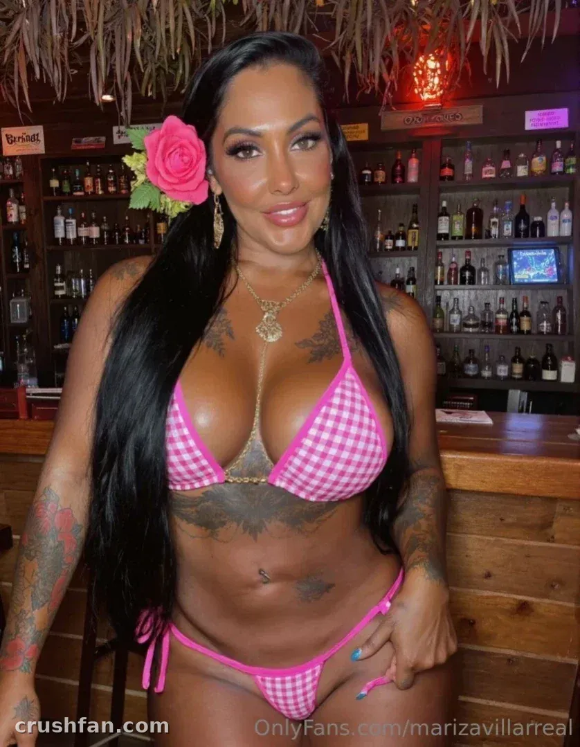 Mariza Villarreal in a pink gingham bikini standing at a bar with a flower in her hair
