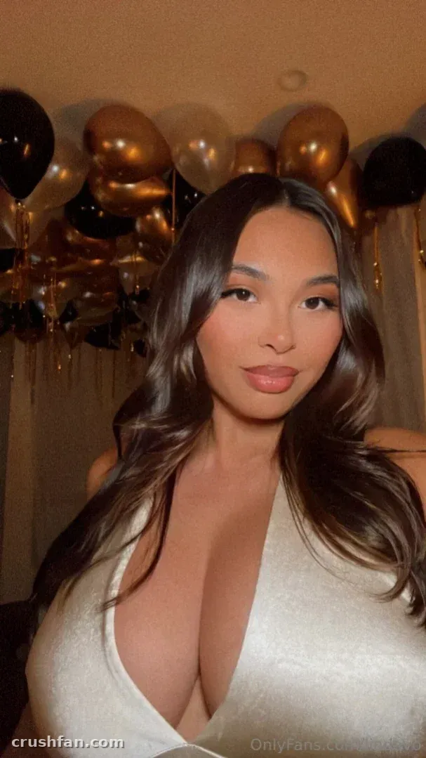 Linda Vo con un top blanco de cuello en V posando frente a globos negros y dorados.