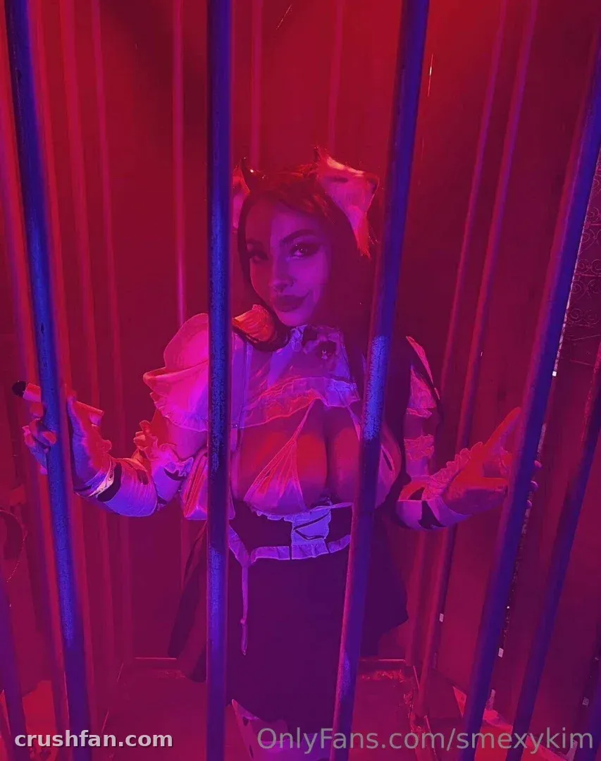Kimmy VIP com uma fantasia de babados atrás das grades sob luz vermelha
