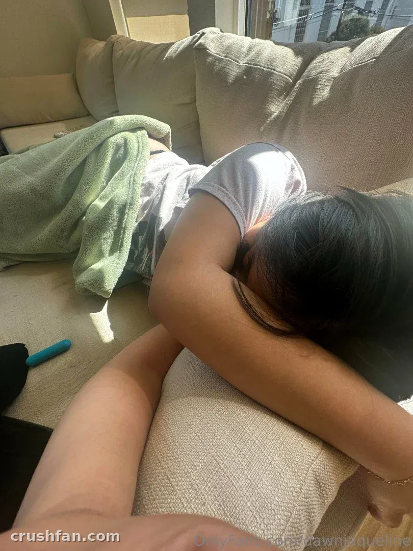 Dawn Jaqueline resting face down on a beige sofa under a green blanket in daylight