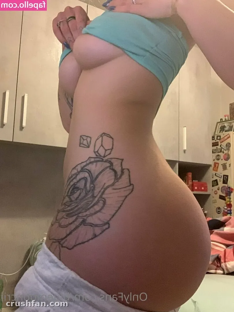 Creator showing a rose hip tattoo while lifting a light blue crop top in a bedroom mirror