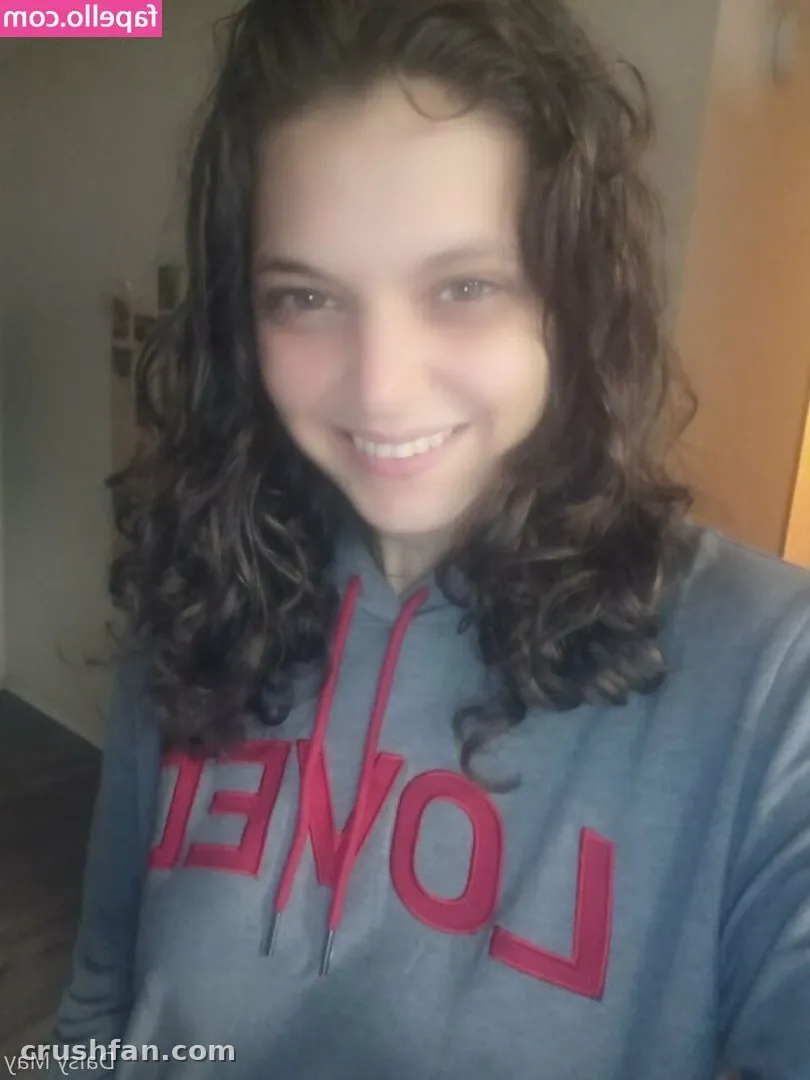 DoItWithDaisy souriant dans un sweat à capuche gris avec des lettres rouges dans un selfie en intérieur