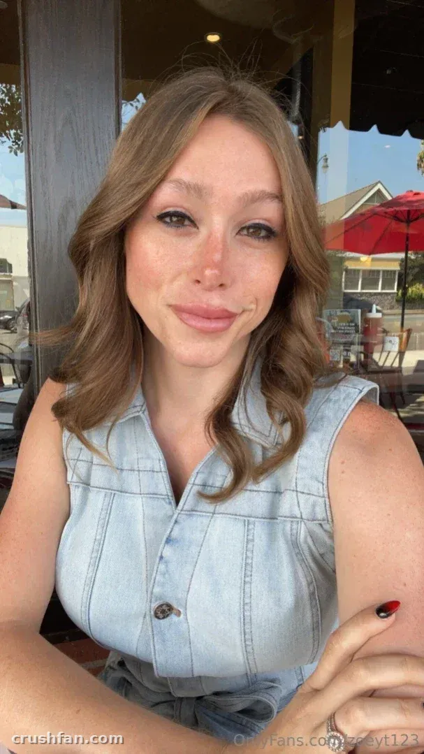 Zoey Taylor con un top de denim azul claro, sentada al aire libre cerca de una ventana.