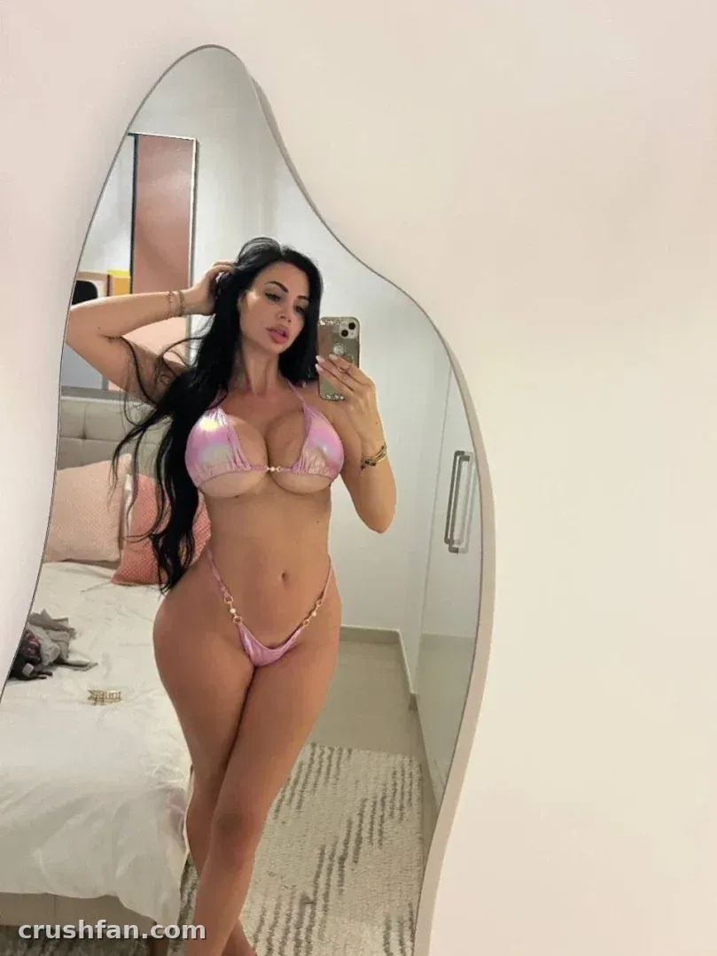 Yvonne Bar tomándose una selfie frente al espejo en bikini rosa dentro de una habitación luminosa.