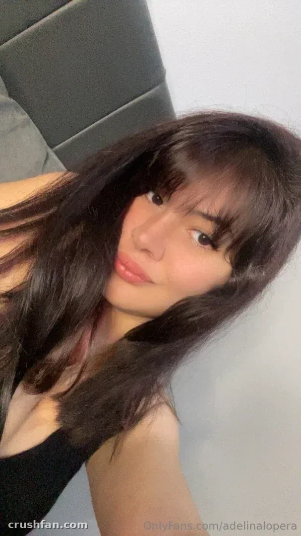Close-up selfie of a woman with long dark layered hair and bangs, wearing a black top indoors.