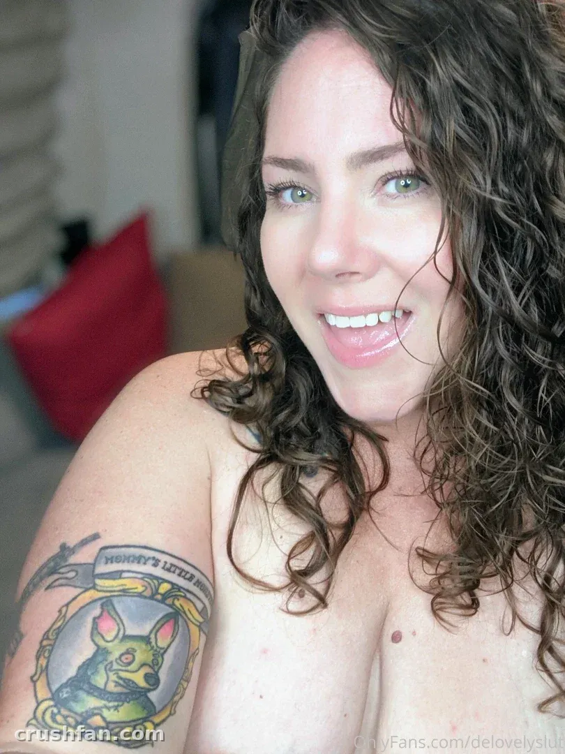 Delovelymomma lächelt drinnen mit lockigem Haar und einem Tattoo am Arm