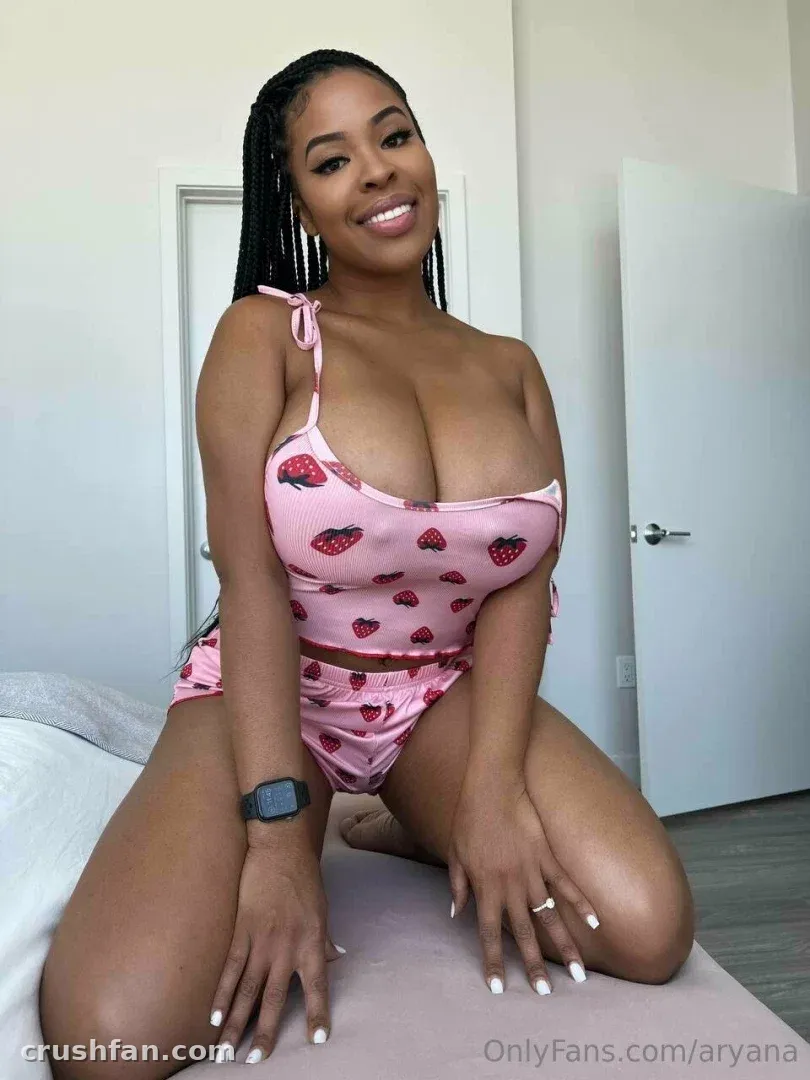 Aryana kneeling on a bed in a pink strawberry print two-piece set, smiling at the camera