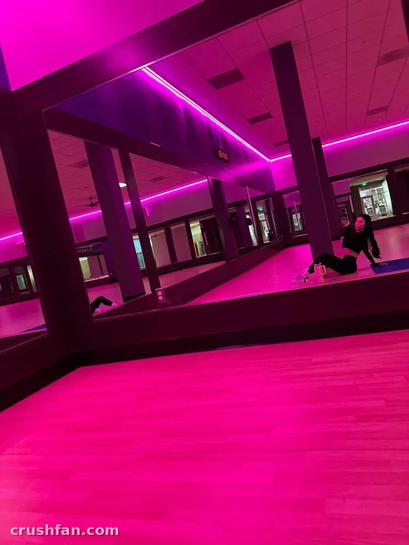 Mujer sentada sobre una esterilla en un estudio iluminado en rosa con paredes espejadas y suelo resplandeciente