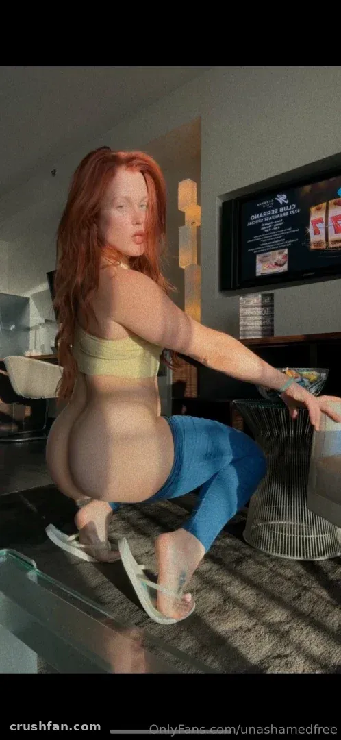 Ash con un top amarillo y leggings azules agachada en una sala de estar luminosa