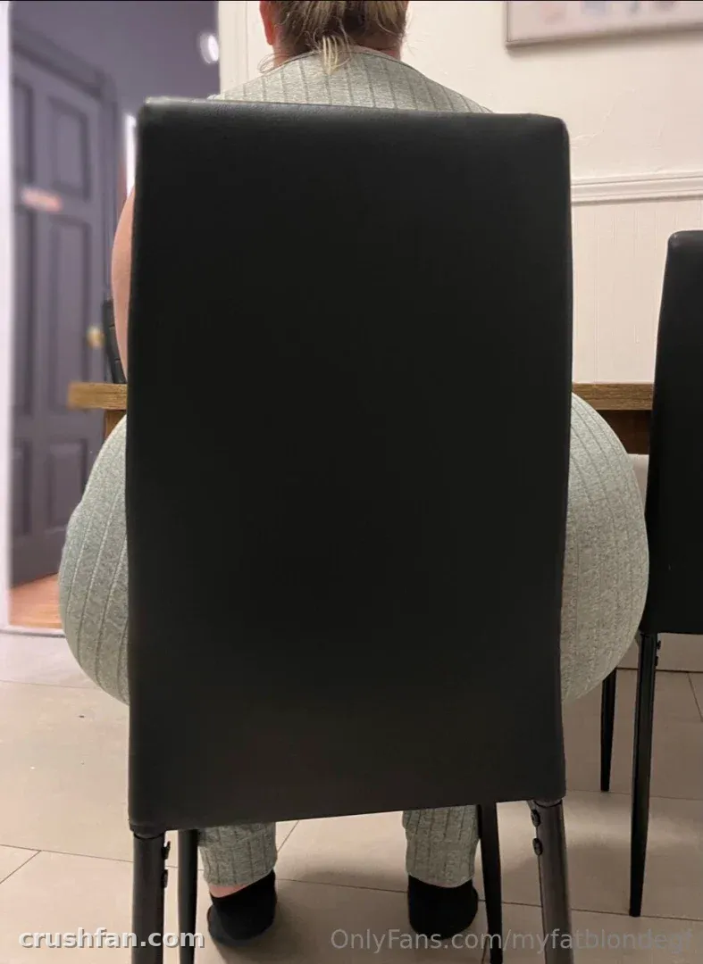 Criador sentado em uma cadeira escura com um conjunto cinza canelado, visto por trás em uma sala clara.