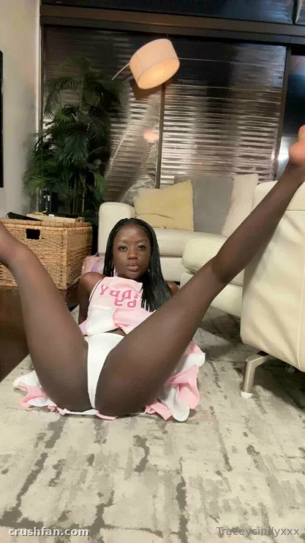 Traceycindyxxx in a pink and white outfit sitting on a grey rug in a living room