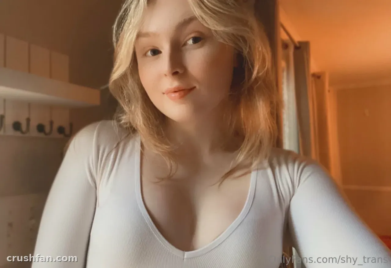 Sarah in a white long-sleeved top taking an indoor selfie in warm light