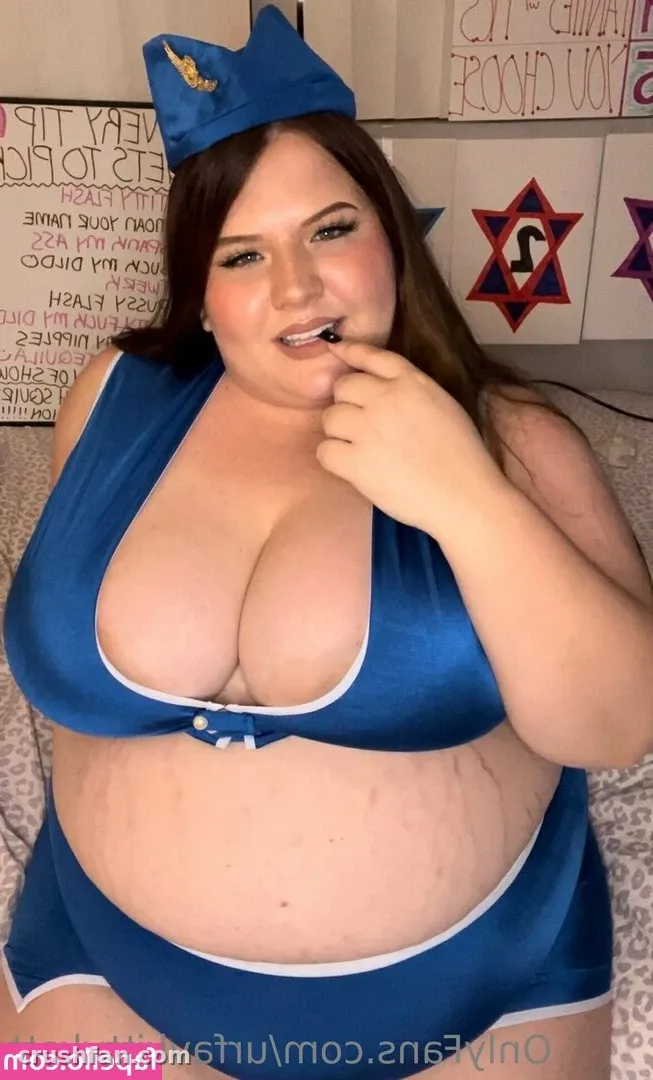 Criadora com um conjunto de duas peças azul e boné combinando, sorrindo em ambiente interno diante de pôsteres.
