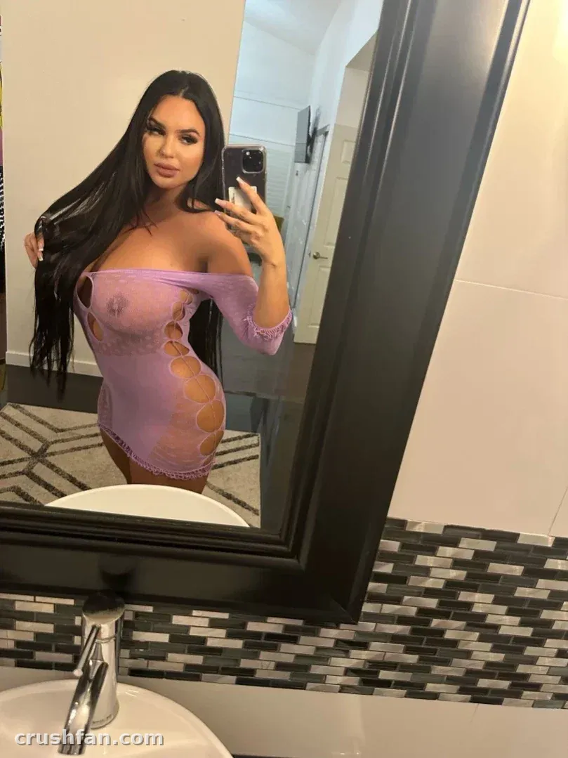 Alexas Morgan in einem lila Cut-out-Kleid, die in einem Badezimmer ein Spiegel-Selfie macht.