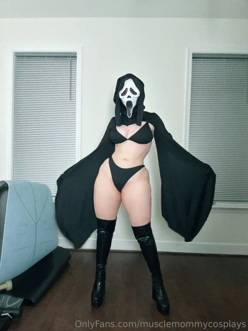 Linnea mit Ghostface-Maske, schwarzem Bikini und Umhang drinnen stehend