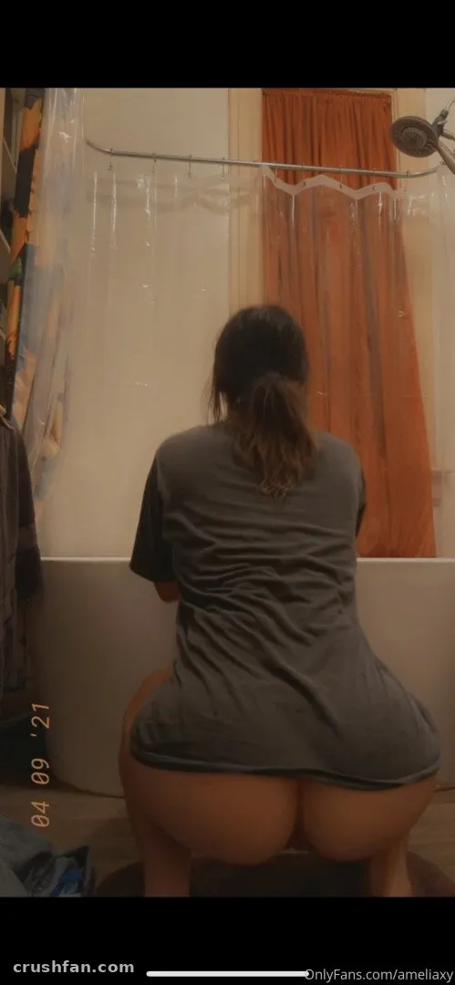 Amelia agachada perto de uma banheira com uma camiseta cinza, vista de costas