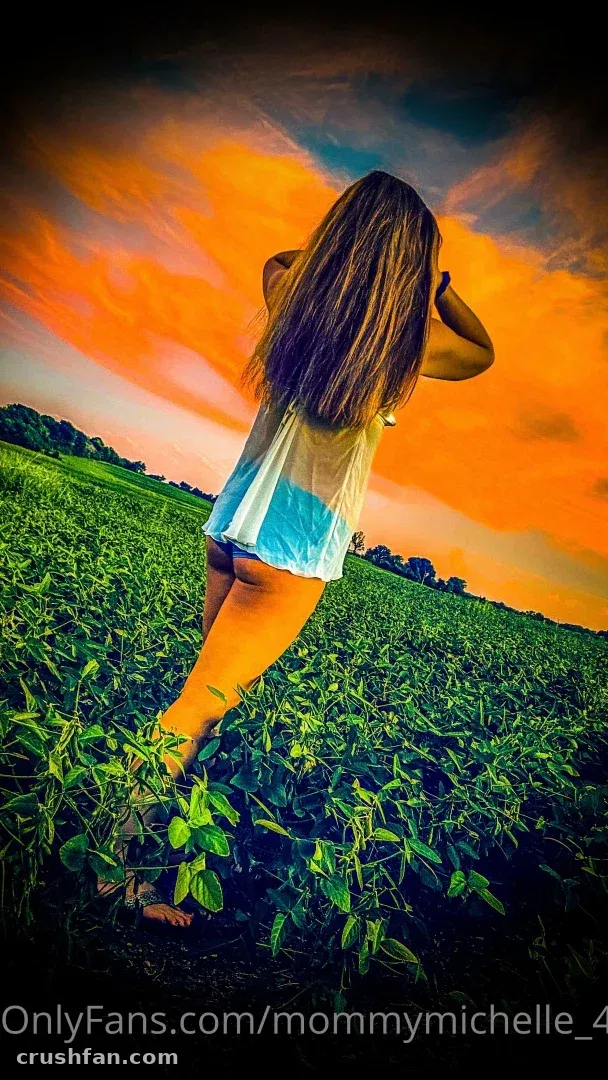 Michelle stands barefoot in a green field beneath a bright orange sky