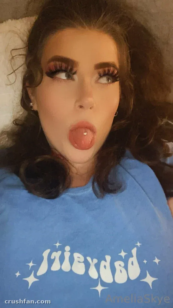 Amelia Skye em uma camiseta gráfica azul fazendo uma careta brincalhona em uma selfie próxima
