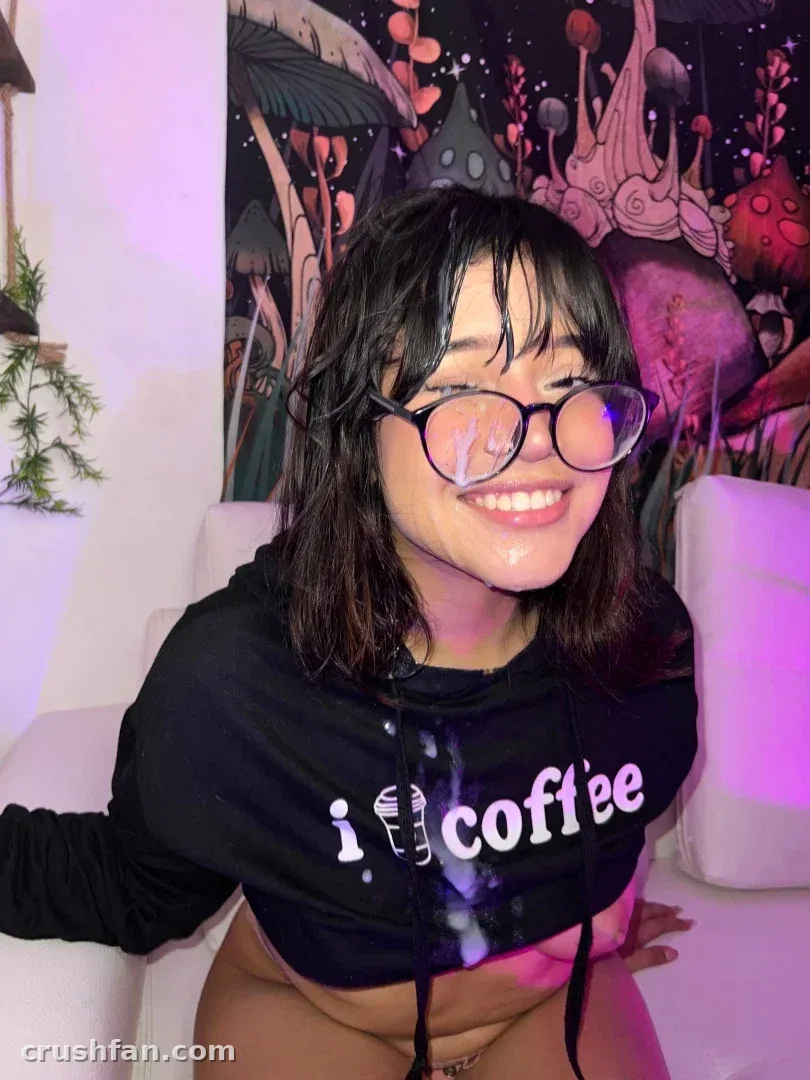 Ana ✧ souriant dans un sweat à capuche noir café et des lunettes rondes en intérieur.