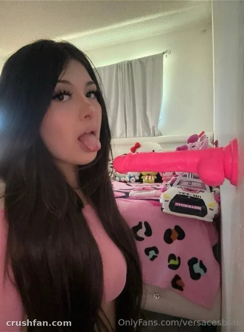 Cherry de blusa rosa em pé em um quarto com bichos de pelúcia e um objeto rosa na parede.