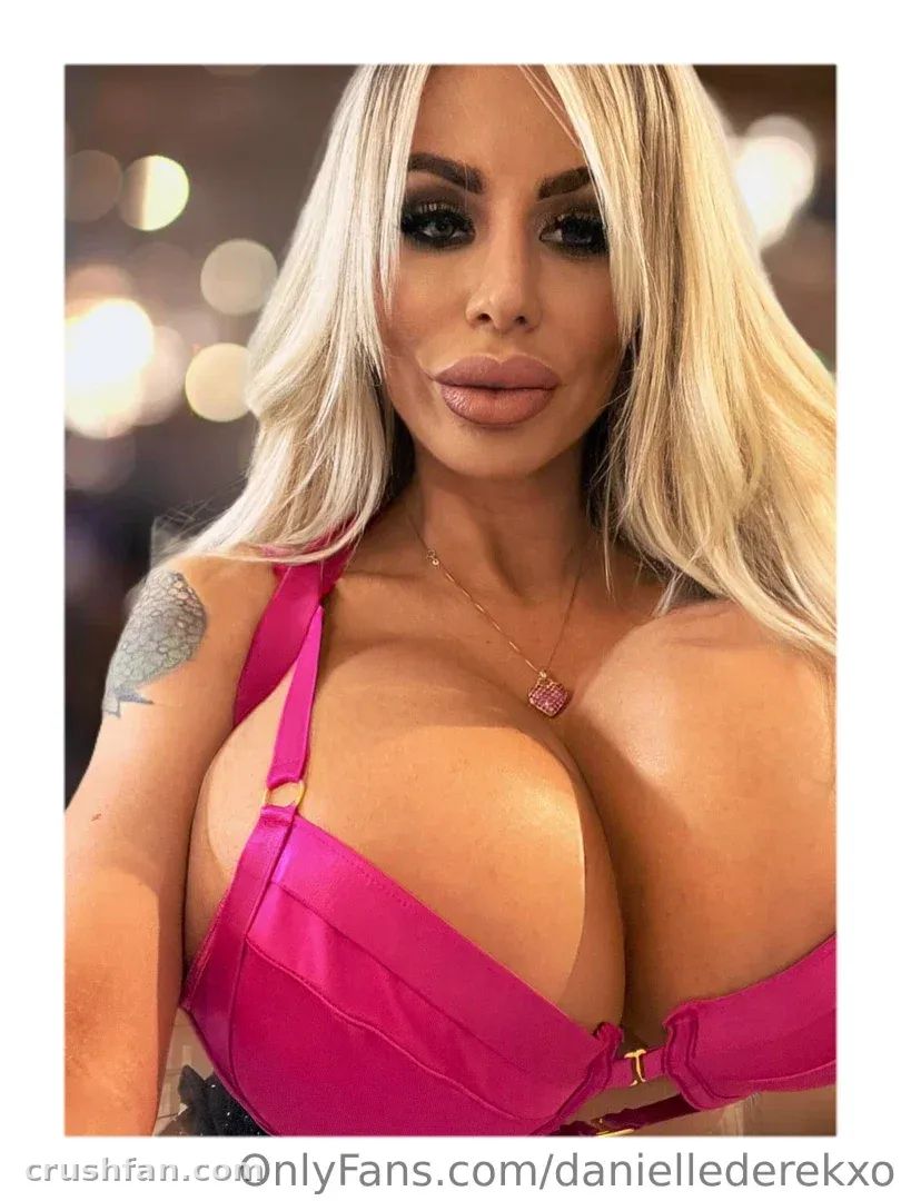 Danielle Derek com uma blusa rosa posando diante de luzes quentes desfocadas