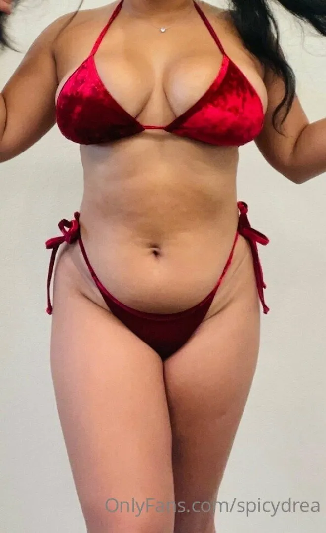 Spicydrea in a shiny red two-piece set against a plain light wall