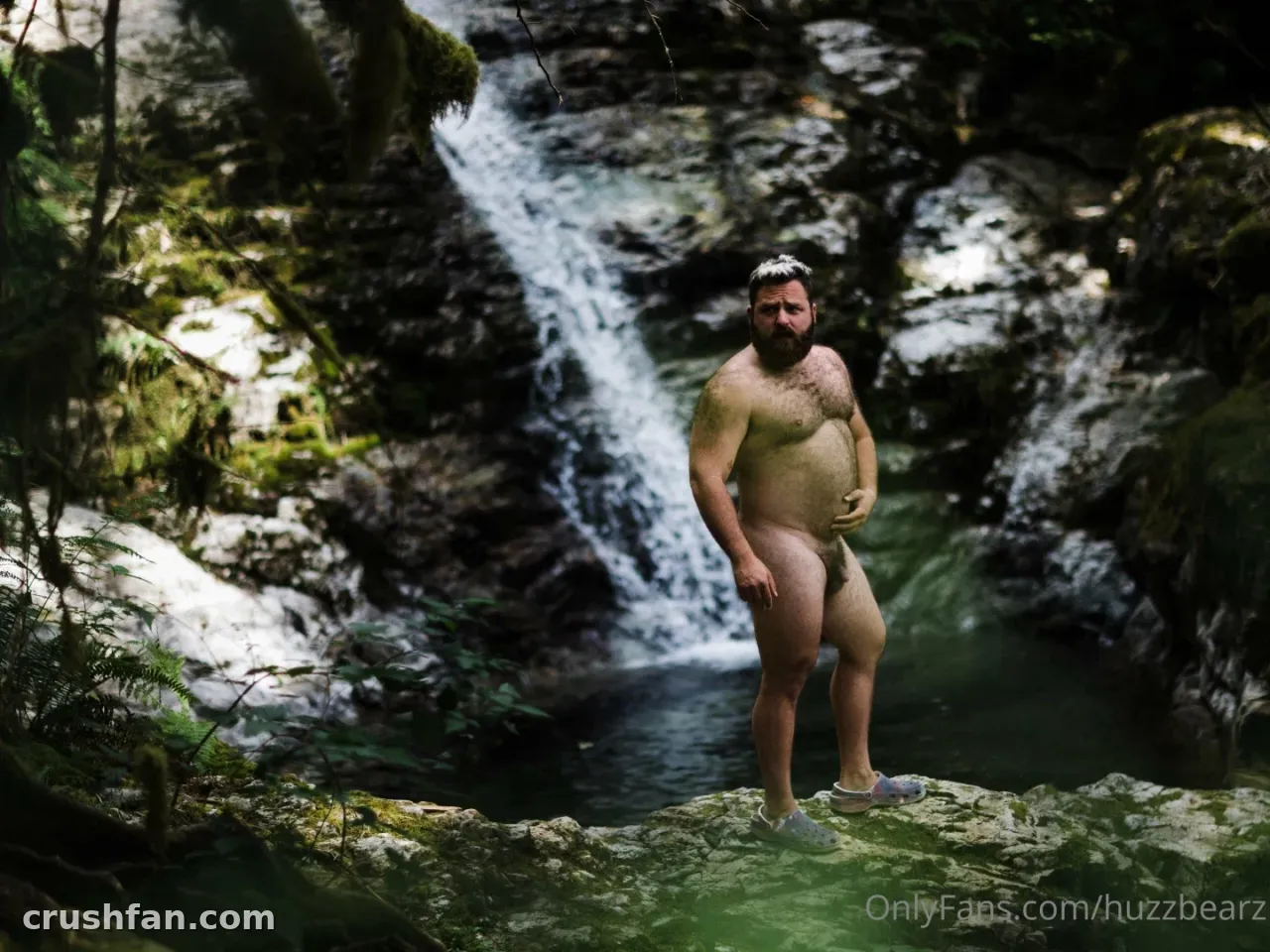 Person steht auf moosigen Felsen vor einem Waldwasserfall