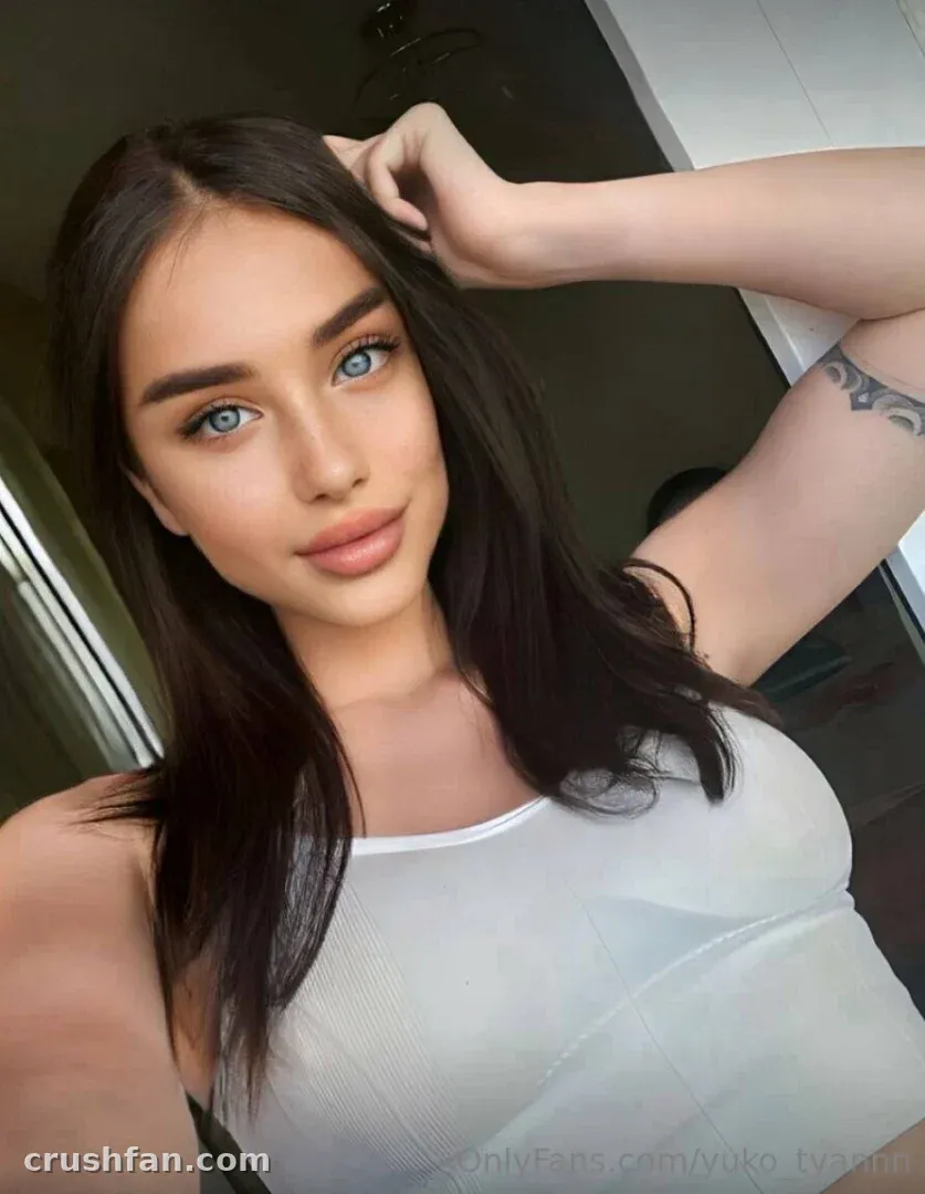 Yuko Tyan con un top blanco tomándose una selfie en primer plano en interiores con un brazo levantado