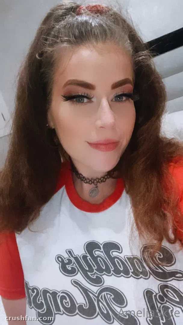 Amelia Skye in a red-trimmed white graphic tee and black choker, close-up selfie.