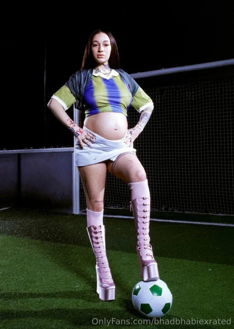 Bhad Bhabie dans un maillot court et des bottes roses debout sur un terrain de football la nuit
