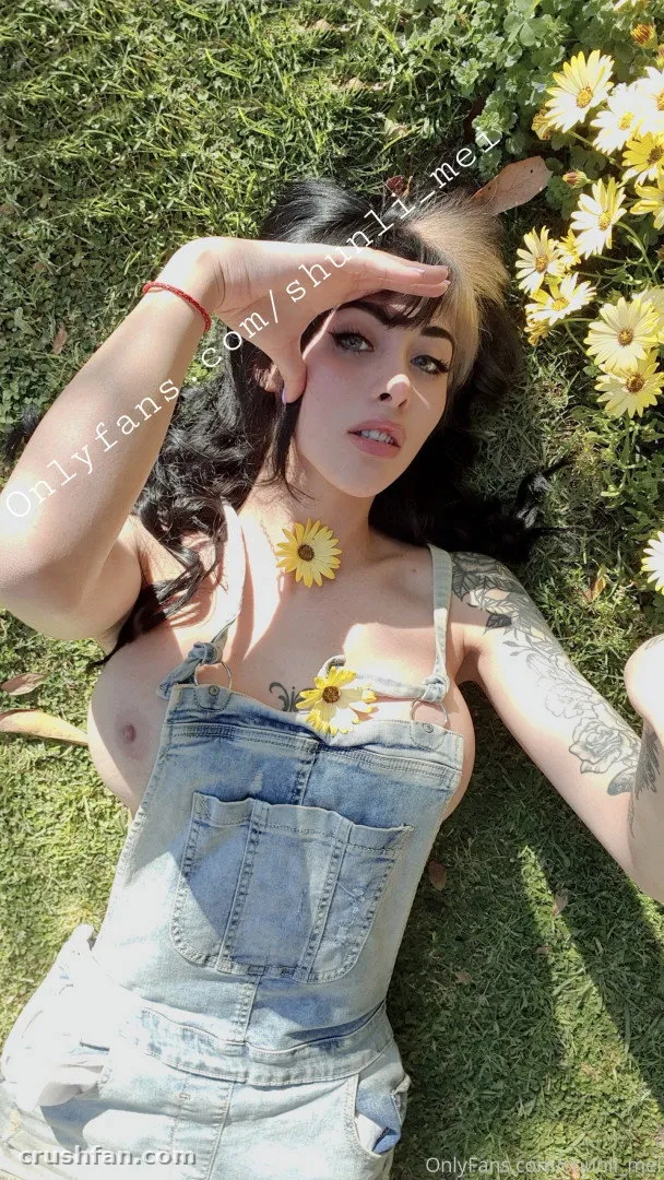 Shunli Mei lying on grass beside sunflowers in denim overalls