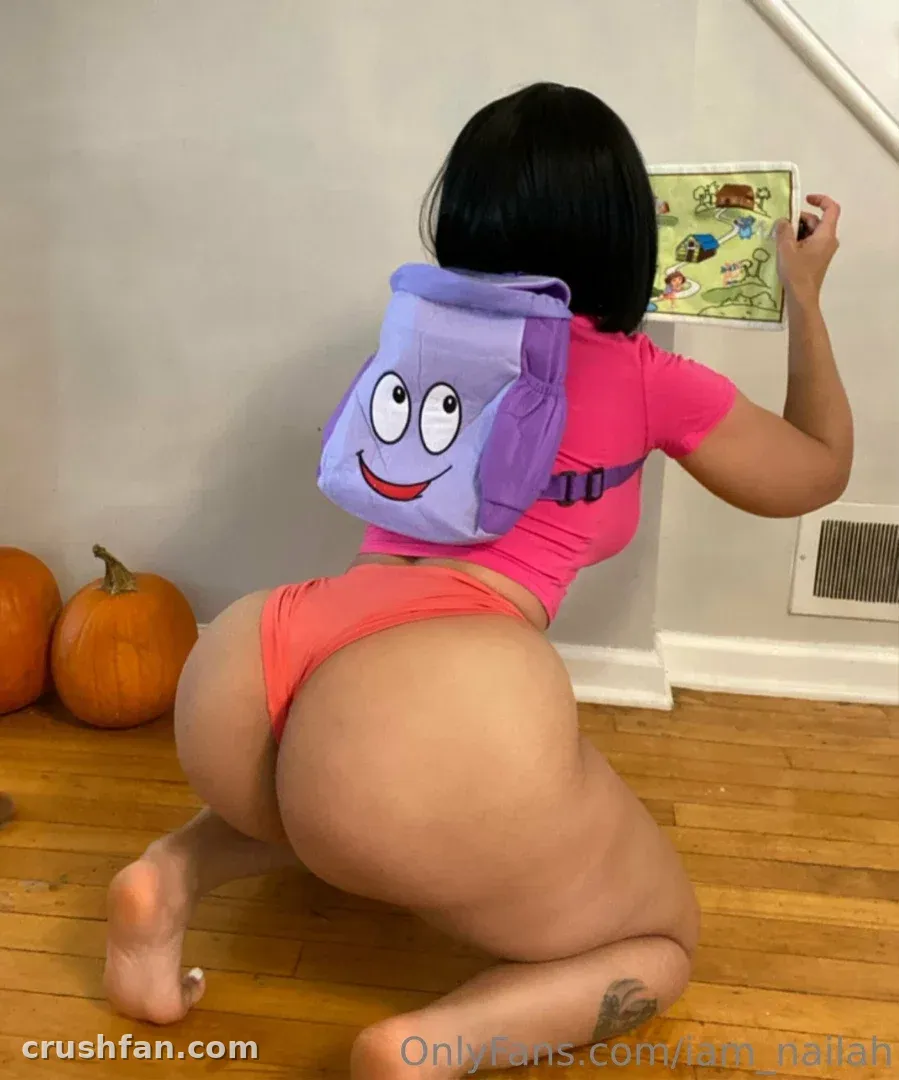 Creator Nailah ajoelhada em um piso de madeira com um look rosa e uma mochila roxa, abóboras por perto