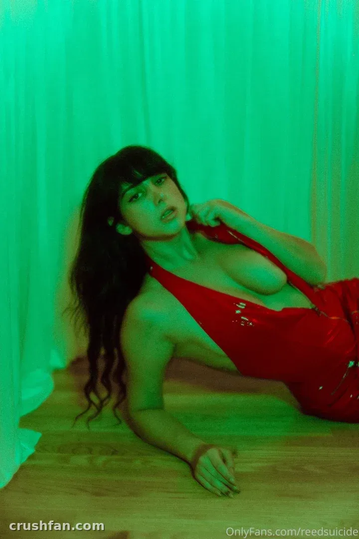Reed in a red latex top lying on a wooden floor before a green curtain