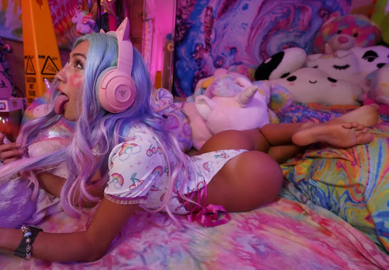 Creator ibabyrainbow liegt auf einem bunten Bett mit Plüschtieren und pinken Kopfhörern
